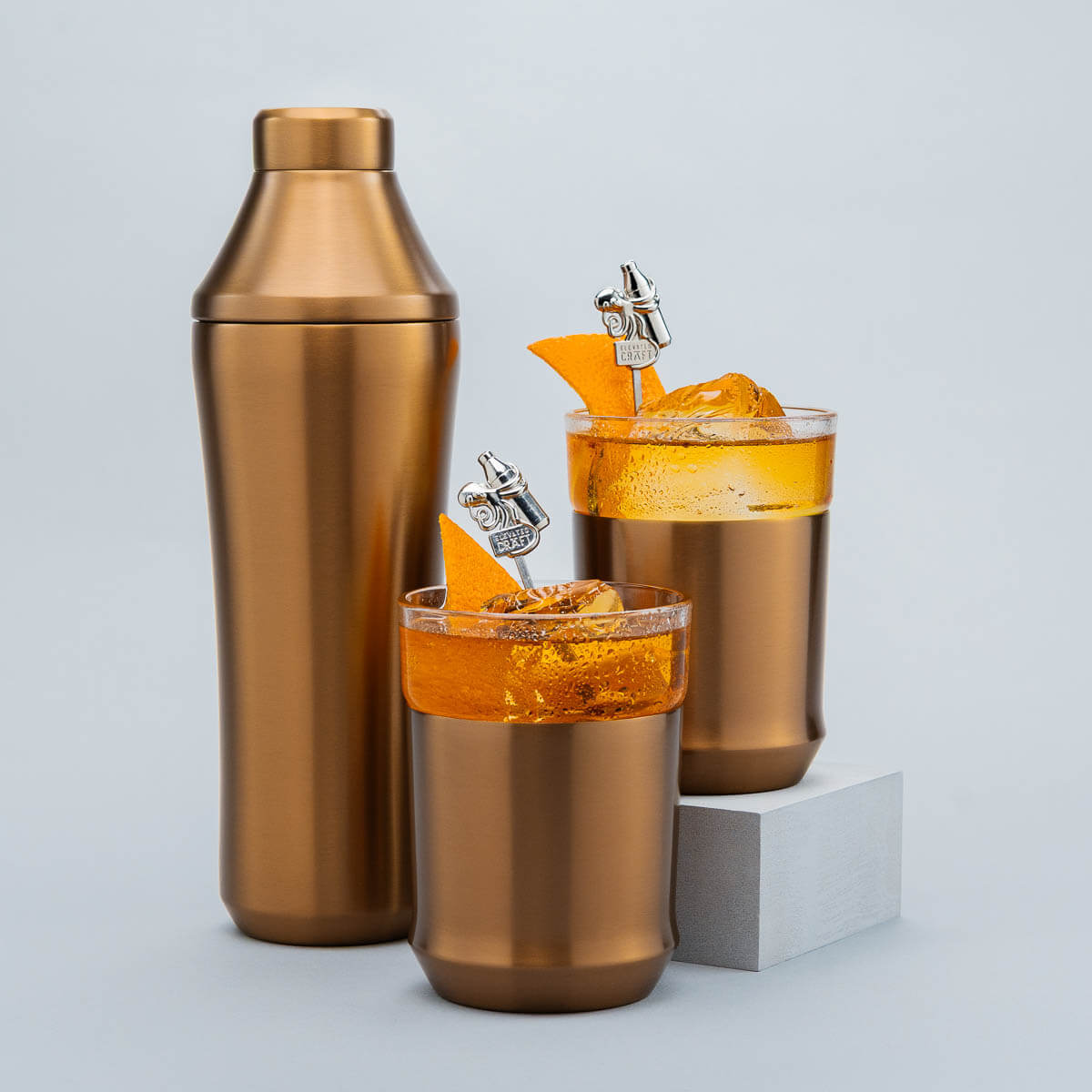 Brushed Copper cocktail shaker and glasses with orange cocktails on a light gray background