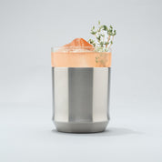 Stainless steel Elevated Craft Hybrid Cocktail Glass filled with bright peach cocktail with an herb garnish