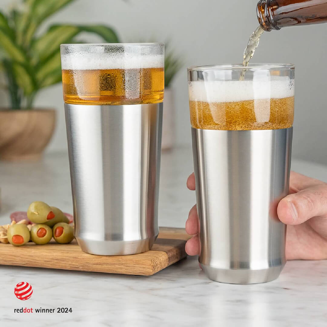 Man pouring cold beer from a bottle into the Elevated Craft Hybrid Pint Glass in brushed stainless finish next to another stainless hybrid pint glass full of cold beer with the 2024 red dot design award badge in the bottom left corner of image