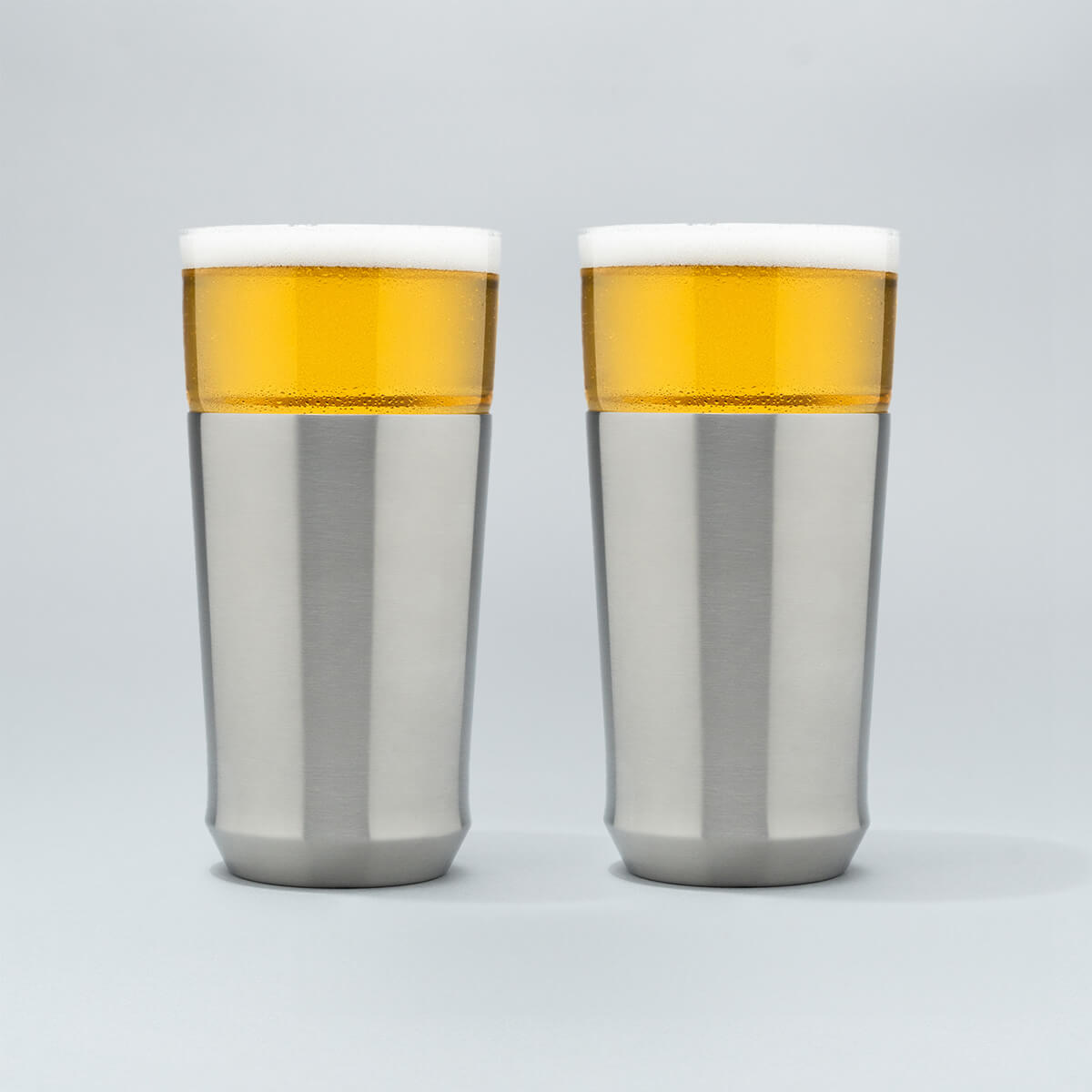 Two Elevated Craft Hybrid Pint Glasses in brushed stainless finish filled with cold beer to the top of their rims