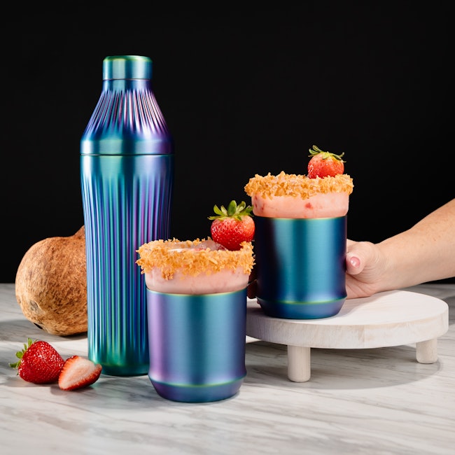 Hand reaches for a creamy drink featuring strawberries and coconut with garnishes of each
