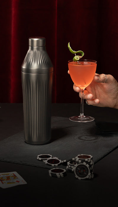 Tattooed arm holding red cocktail with lime peel garnish next to the Gunmetal Black Elevated Craft Diamond Edition Hybrid Cocktail Shaker