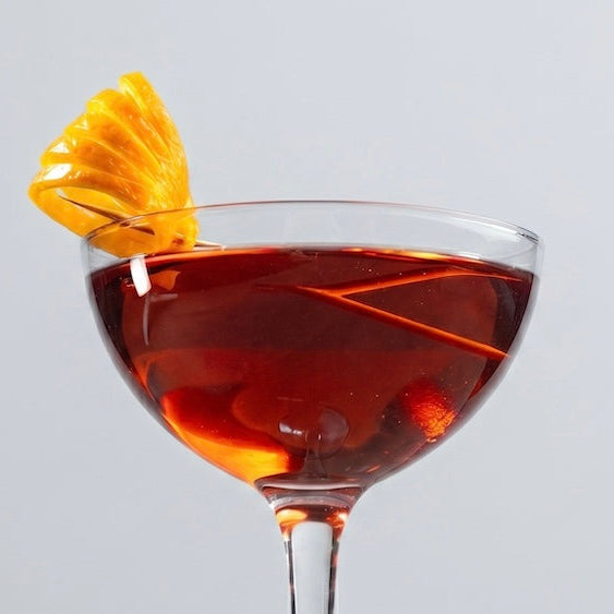 Red cocktail in glass with orange peel garnish