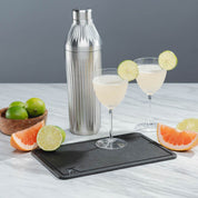 Photo of cut fruit on a white marble counter using the elevated craft cutting board with the Diamond Edition Cocktail Shaker and 2 coup glasses