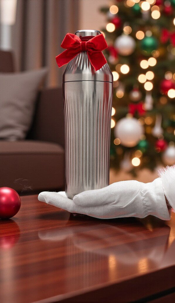 Silver cocktail shaker with a red bow held by a gloved hand in front of a Christmas tree.