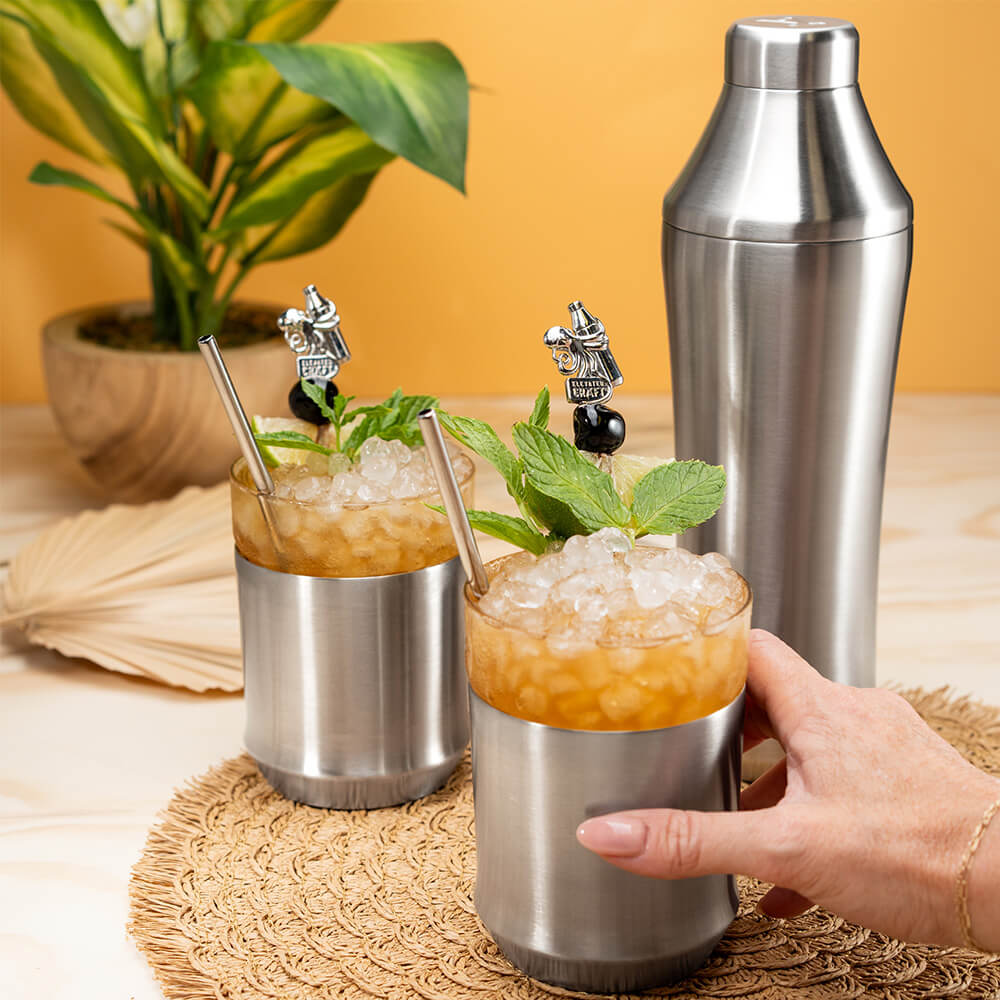 Hand holding Stainless Steel Elevated Craft Hybrid Cocktail Glass with drink in it topped with mint and cherry on a Premium Cocktail Pick next to the Hybrid Cocktail Shaker