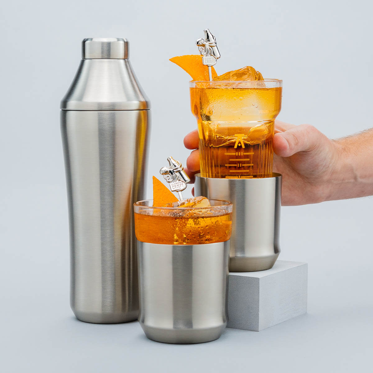 Cocktail shaker and glasses with orange cocktails on a light gray background
