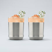 Two Stainless steel Elevated Craft Hybrid Cocktail Glasses filled with bright peach cocktails with herb garnishes
