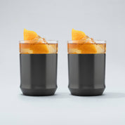 two gunmetal black finish Elevated Craft hybrid cocktail glasses filled with amber cocktails large ice cubes and garnished with orange peels