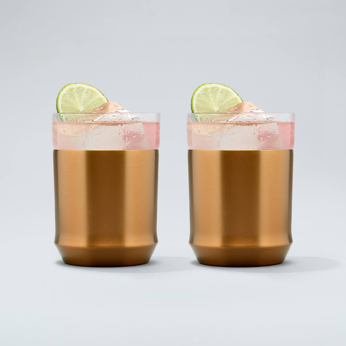 two brushed copper Elevated Craft hybrid cocktail glasses filled with a bright pink cocktail large ice cubes and lime wheel garnishes