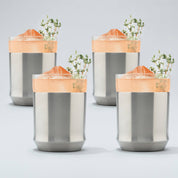 Four Stainless steel Elevated Craft Hybrid Cocktail Glasses filled with bright peach cocktails large ice cubes and herb garnishes