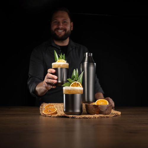 Bartender holding a cocktail with garnishes on a dark background