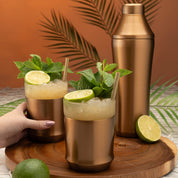 Hand holding the Elevated Craft Brushed Stainless Hybrid Cocktail Glass filled with Mai Tai cocktail topped with spent lime and mint next to the Hybrid Cocktail Shaker