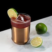 Elevated Craft Brushed Copper Hybrid Cocktail Glass filled with dark red cocktail topped with lime slice next to limes on countertop