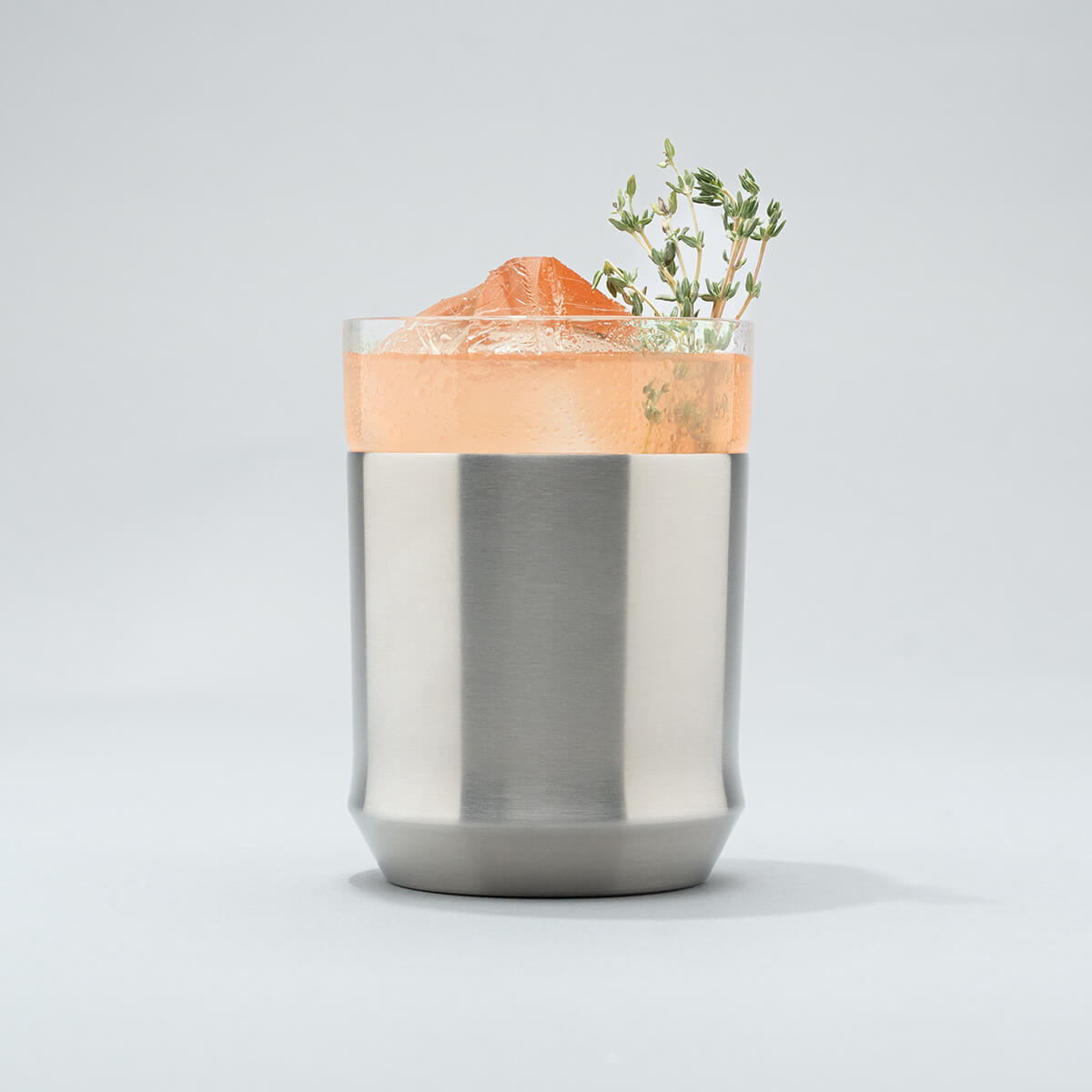 Stainless steel Elevated Craft Hybrid Cocktail Glass filled with bright peach cocktail with an herb garnish