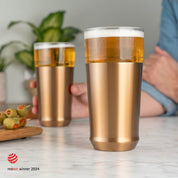 An Elevated Craft Hybrid Pint Glass in brushed copper finish full of cold beer in foreground with a hand holding a brushed copper hybrid pint glass insert full of cold beer in the background with the 2024 red dot design award logo overlaid in the bottom left corner