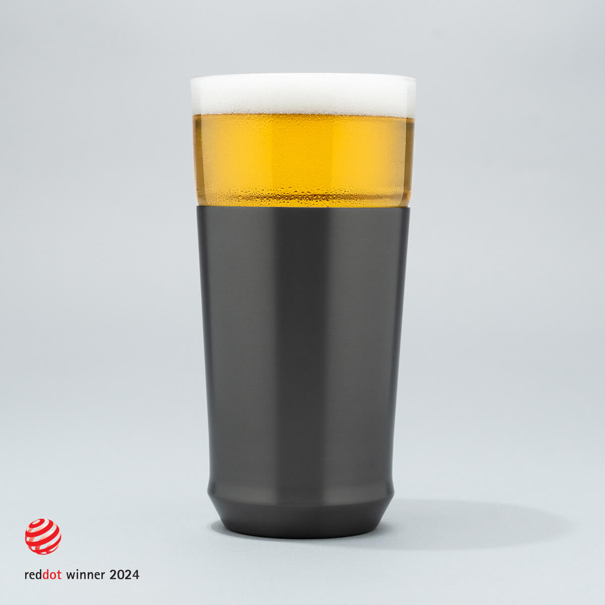 The Elevated Craft Hybrid Pint Glass in gunmetal black finish filled with cold beer to the top of the rim with the 2024 red dot design award logo overlaid in the bottom left corner