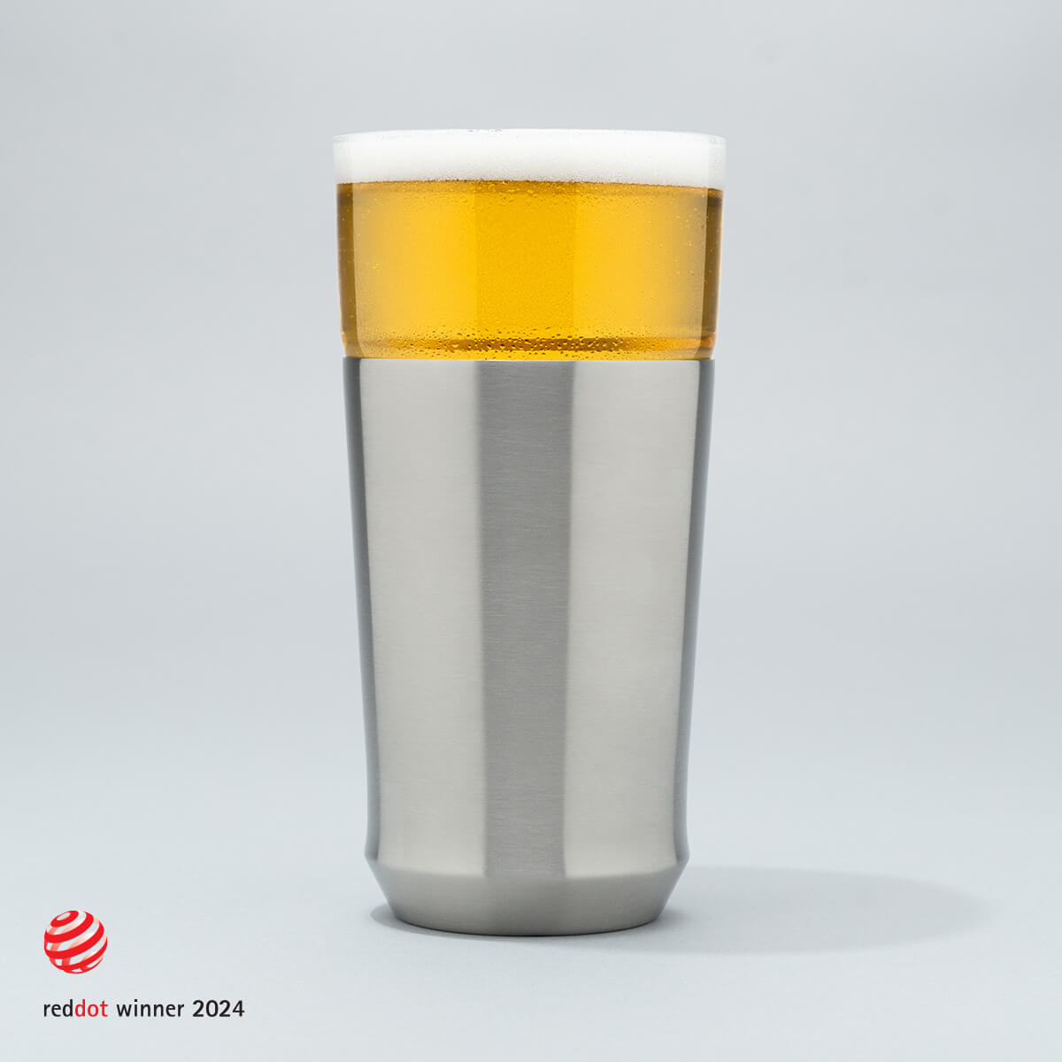 The Elevated Craft Hybrid Pint Glass in Brushed Stainless Finish filled with cold beer to the top of the rim with the 2024 red dot design award logo overlaid in the bottom left corner