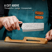 Person holding a knife with a black handle, wearing a blue apron, on a wooden surface.