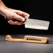 Hand holding a hammered steel knife over a wooden stand on a dark background