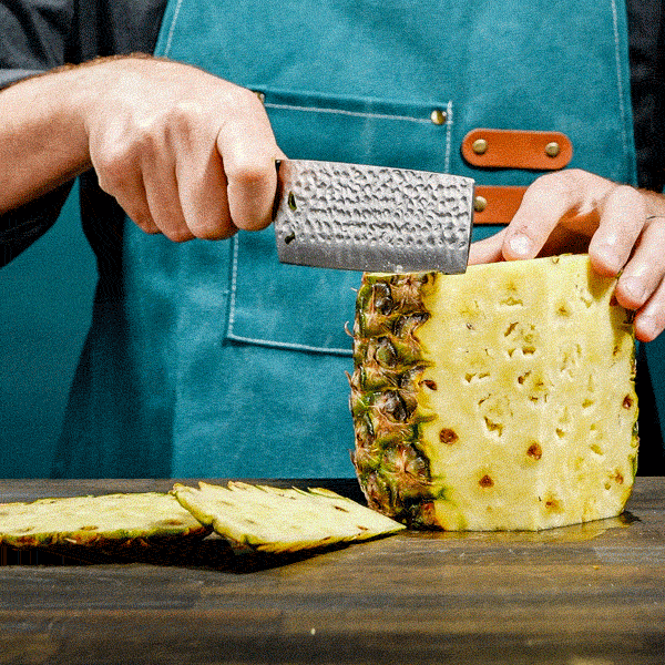 Person using a nakiri knife, cutting a pineapple on a wooden surface