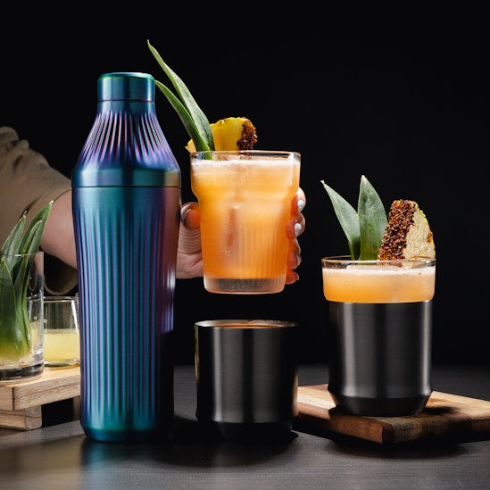 Cocktail shaker and glasses with drinks on a dark surface