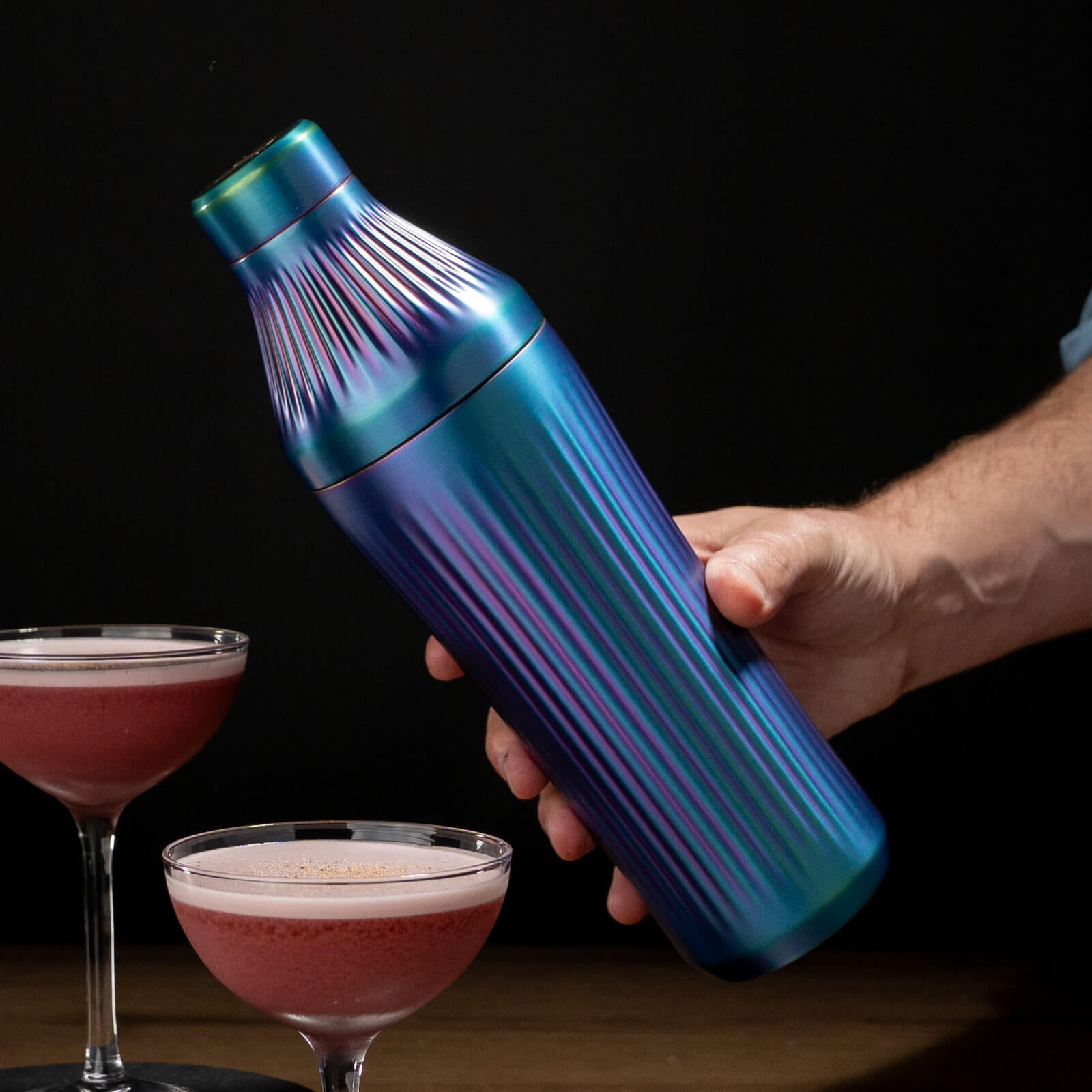 Iridescent cocktail shaker held by a hand with two cocktails in the background