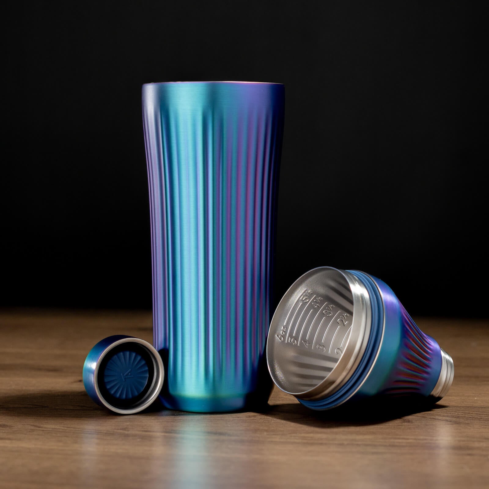 Iridescent  metallic tumbler with two lids on a wooden surface