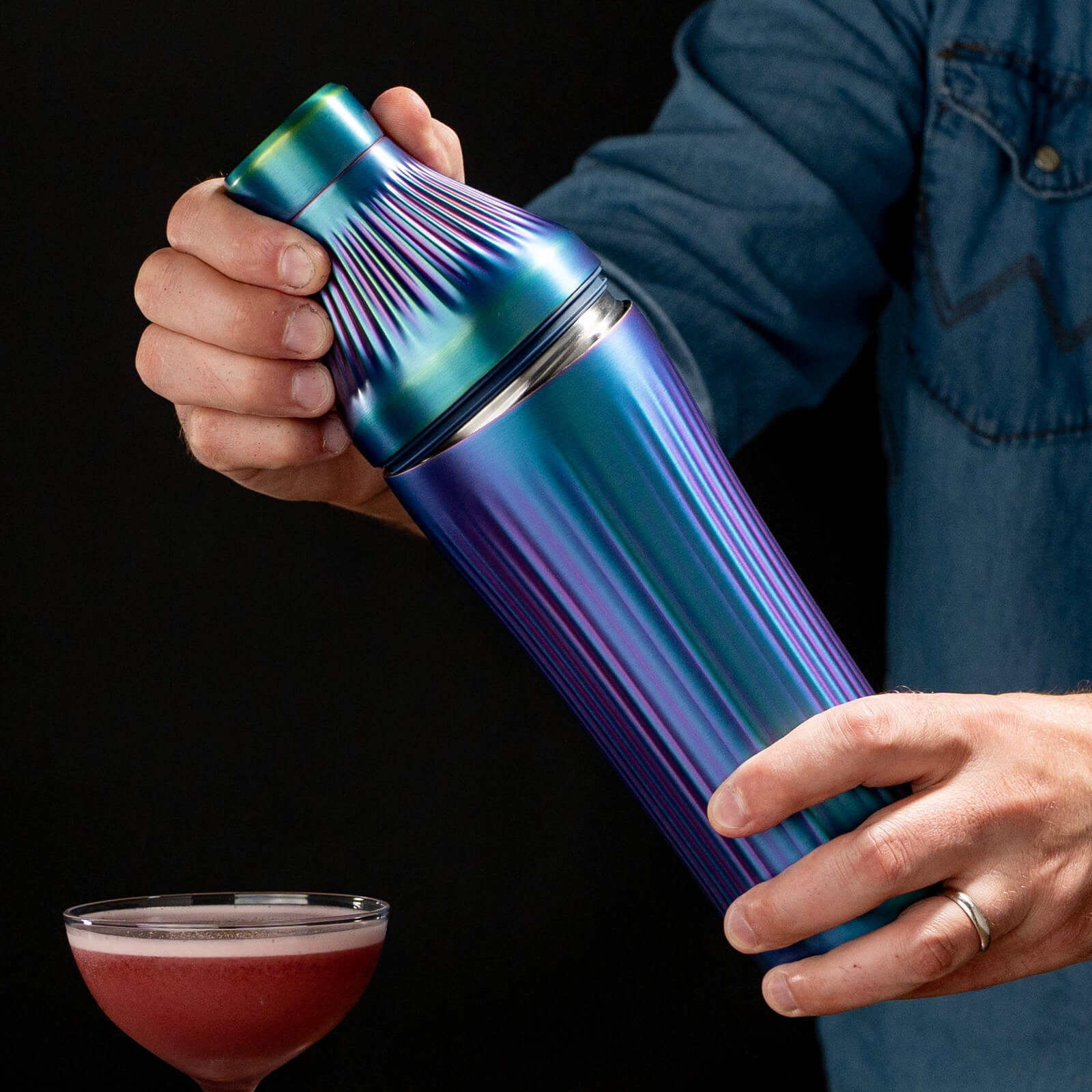 Person holding a metallic Iridescent cocktail shaker with a dark background