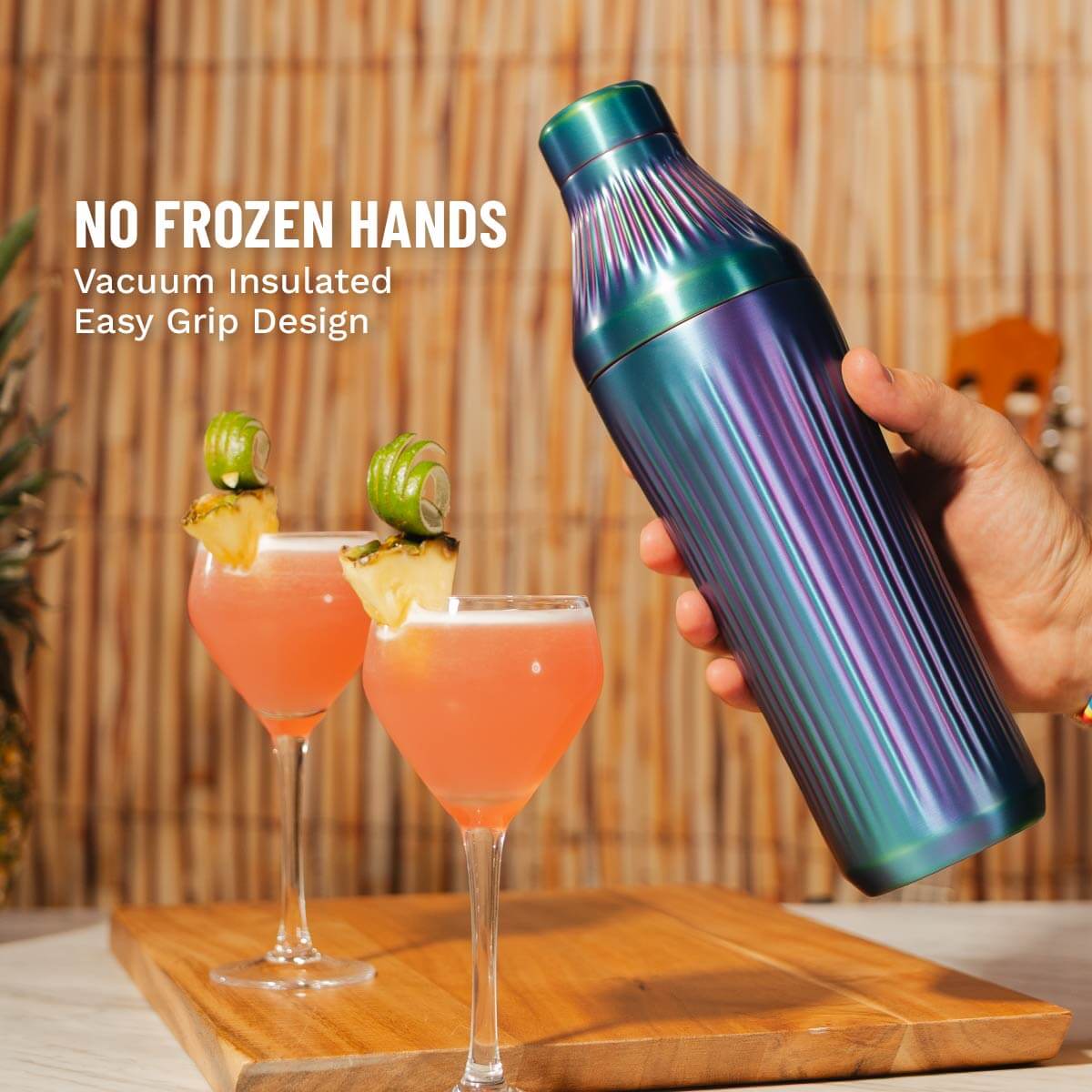 Vacuum insulated bottle with colorful design held over two cocktails on a wooden surface.