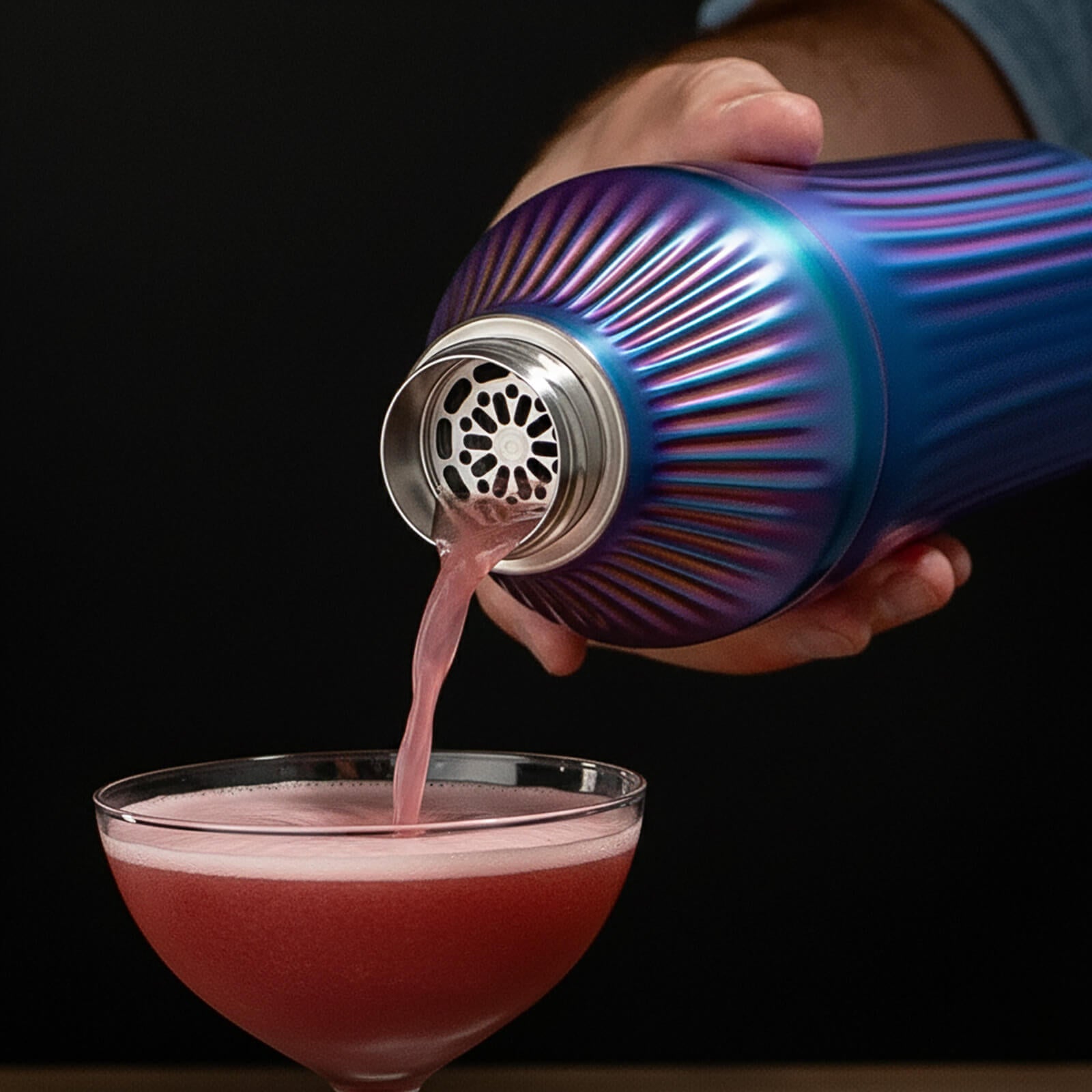 Iridescent  cocktail shaker being used to pour a pink drink into a glass against a black background
