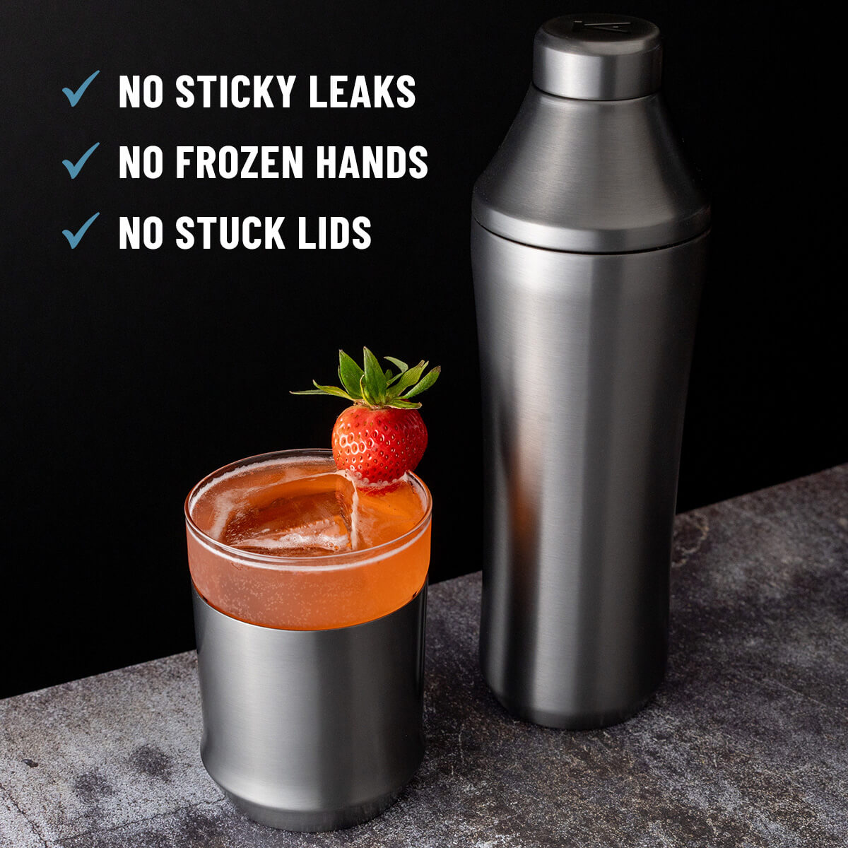 Elevated Craft Gunmetal Black Hybrid Cocktail Shaker next to red cocktail in the Hybrid Cocktail Glass topped with a strawberry with callouts "No sticky leaks, no frozen hands, no stuck lids"