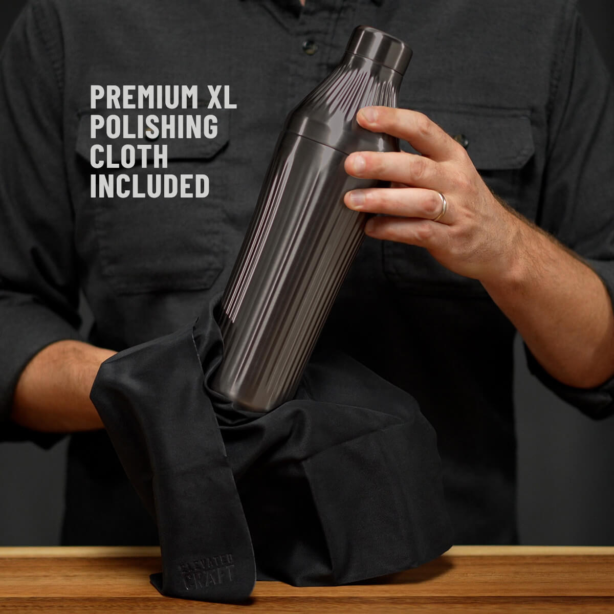 Man in dark grey button down shirt holding the Brushed Stainless Elevated Craft Diamond Edition Hybrid Cocktail Shaker being polished with a Premium XL Polishing Cloth with callout saying Polishing Cloth is included