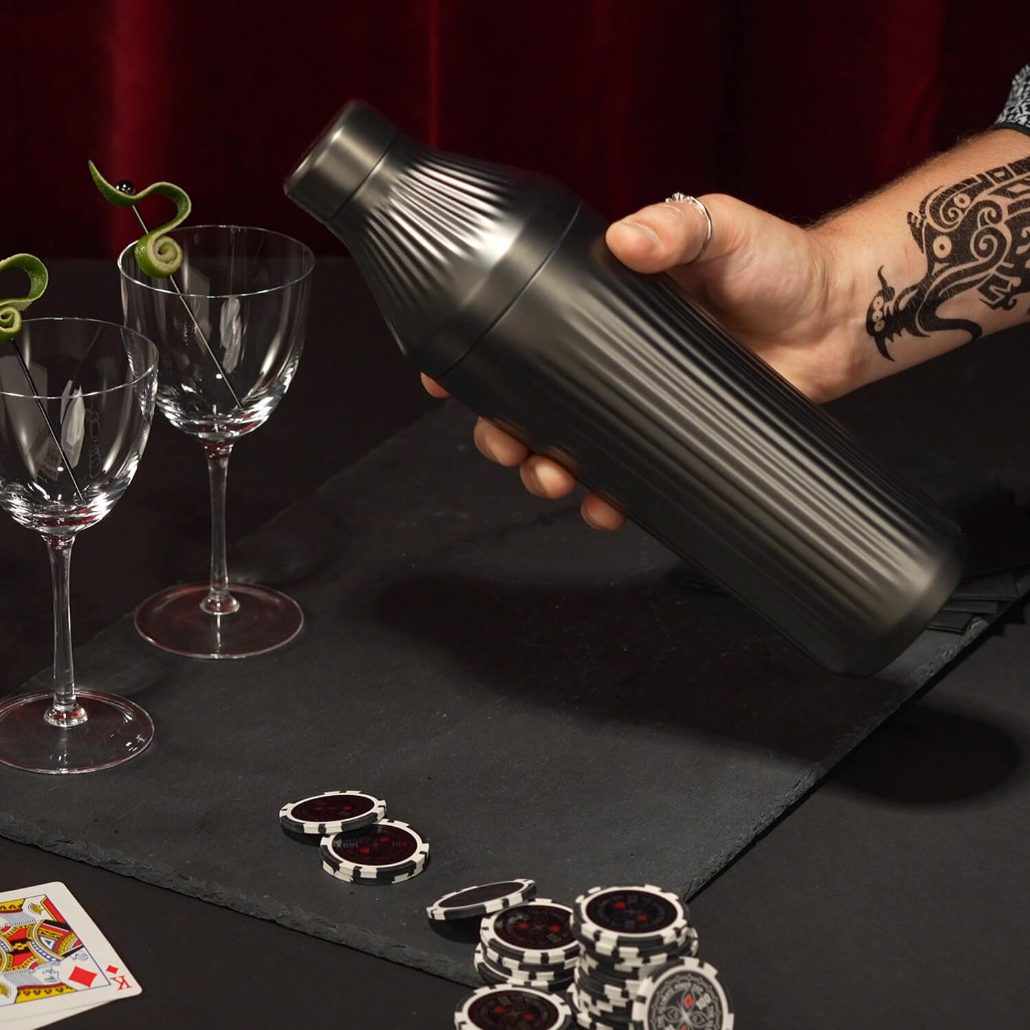A hand holding a Hybrid Cocktail Shaker surrounded by empty glasses