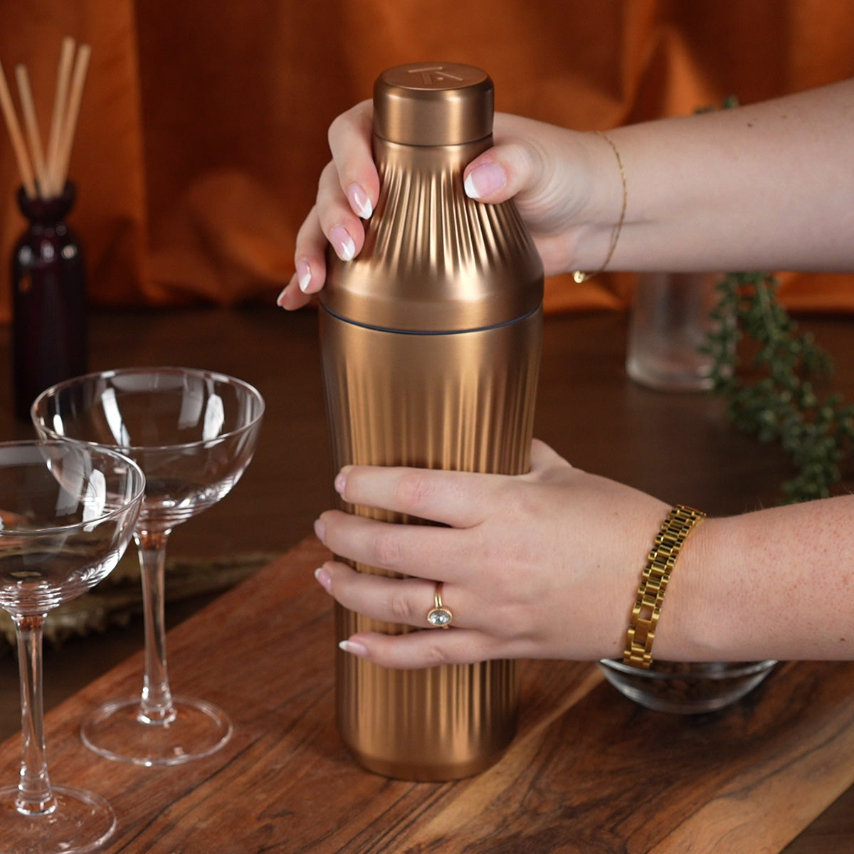 Woman&#39;s hand opening Brushed Copper Elevated Craft Diamond Edition Hybrid Cocktail Shaker measuring top next to empty couple glasses