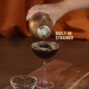 Hand pouring espresso martini through strainer of Brushed Copper Elevated Craft Diamond Edition Hybrid Cocktail Shaker into coupe glass
