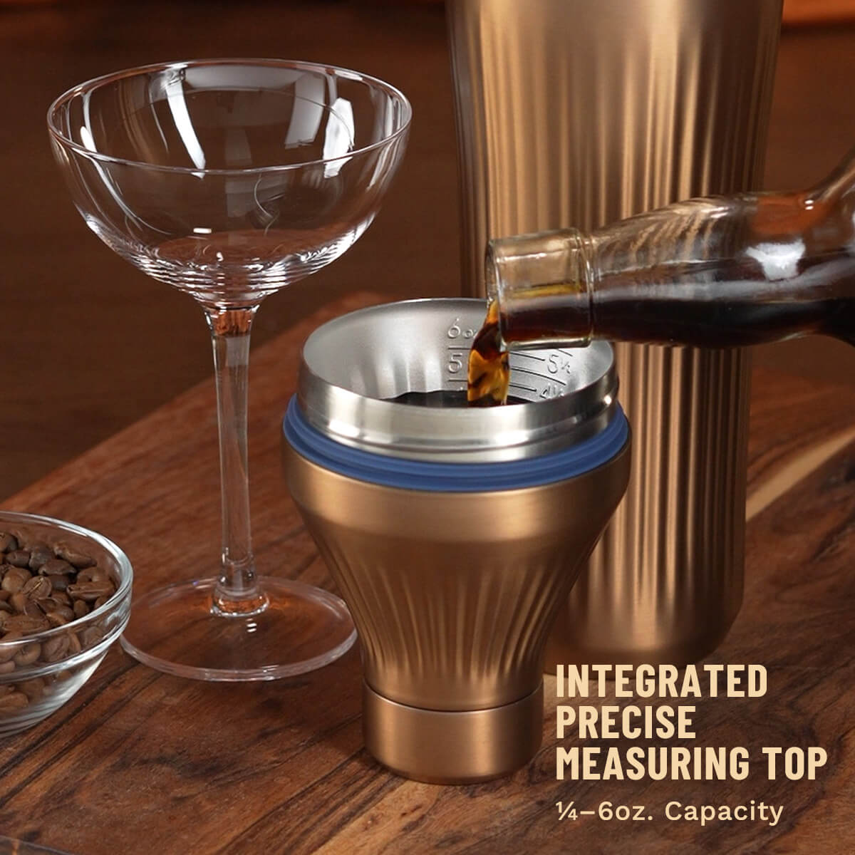 Bottle pouring brown liquid into Brushed Coper Elevated Craft Diamond Edition Hybrid Cocktail Shaker measuring top next to tumbler and empty coupe glass