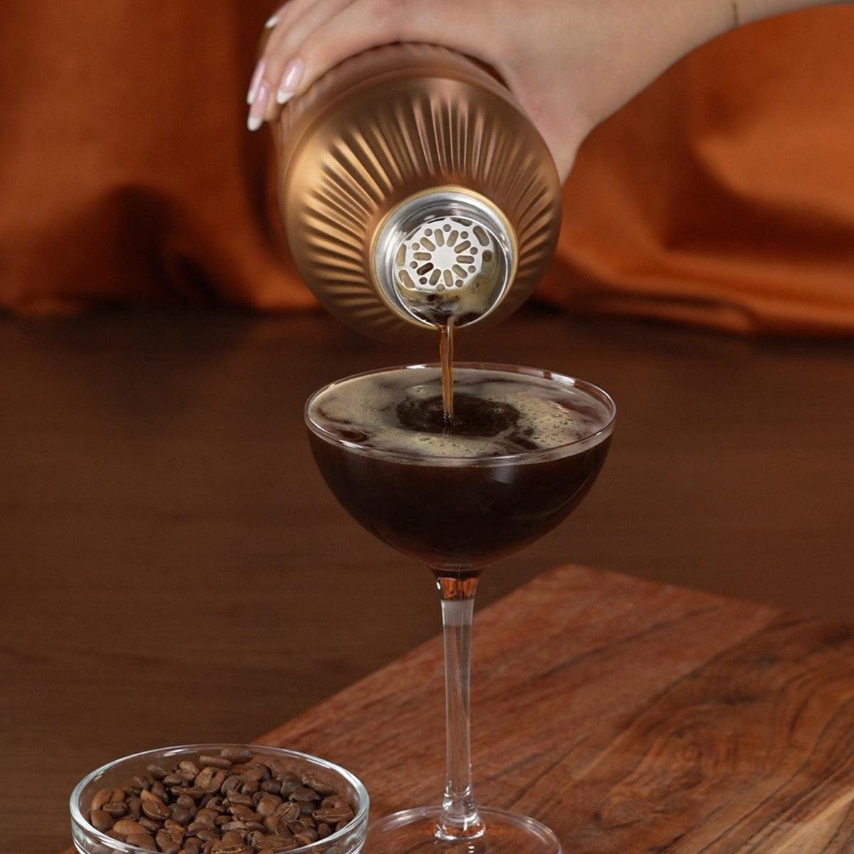 Hand pouring espresso martini through strainer of Brushed Copper Elevated Craft Diamond Edition Hybrid Cocktail Shaker into coupe glass