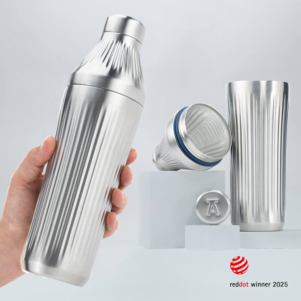 Hand holding a Stainless Steel Diamond Edition Hybrid Cocktail Shaker with another image of the shaker taken apart to show the parts separate on gray background with RedDot Winner 2025 logo overlay