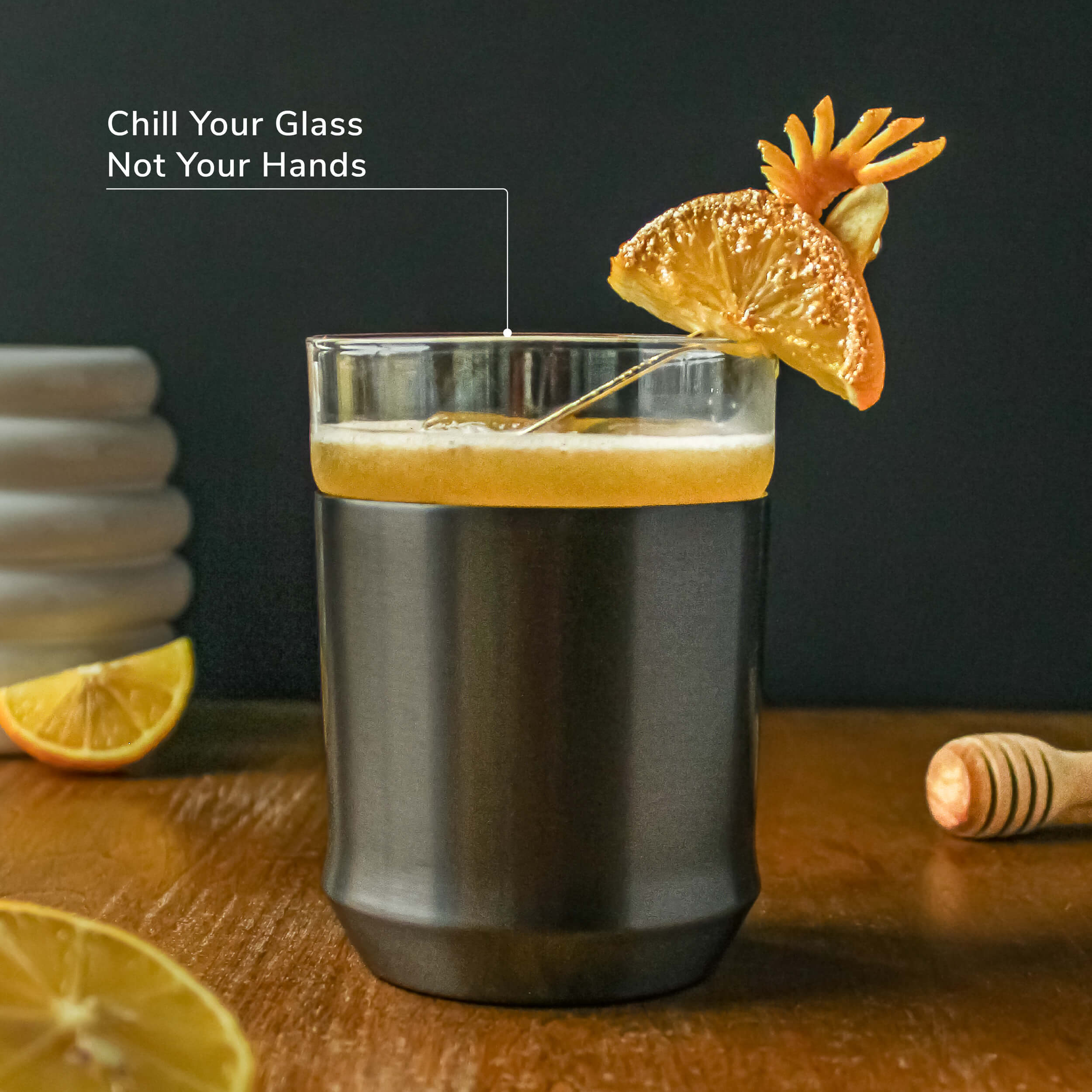 The Elevated Craft hybrid cocktail glass in gunmetal black finish filled with a cloudy orange cocktail chilled by a large ice cube and garnished by a sugar-crusted candied orange slice and fresh orange peel on a gold cocktail pick