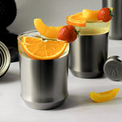 Two Elevated Craft Hybrid Cocktail Glasses in Gunmetal Black finish filled with a bright yellow cocktail large ice cubes and fresh fruit garnishes 