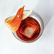 The Elevated Craft hybrid cocktail glass viewed from above filled with a dark orange cocktail and single large ice cube garnished with an orange peel