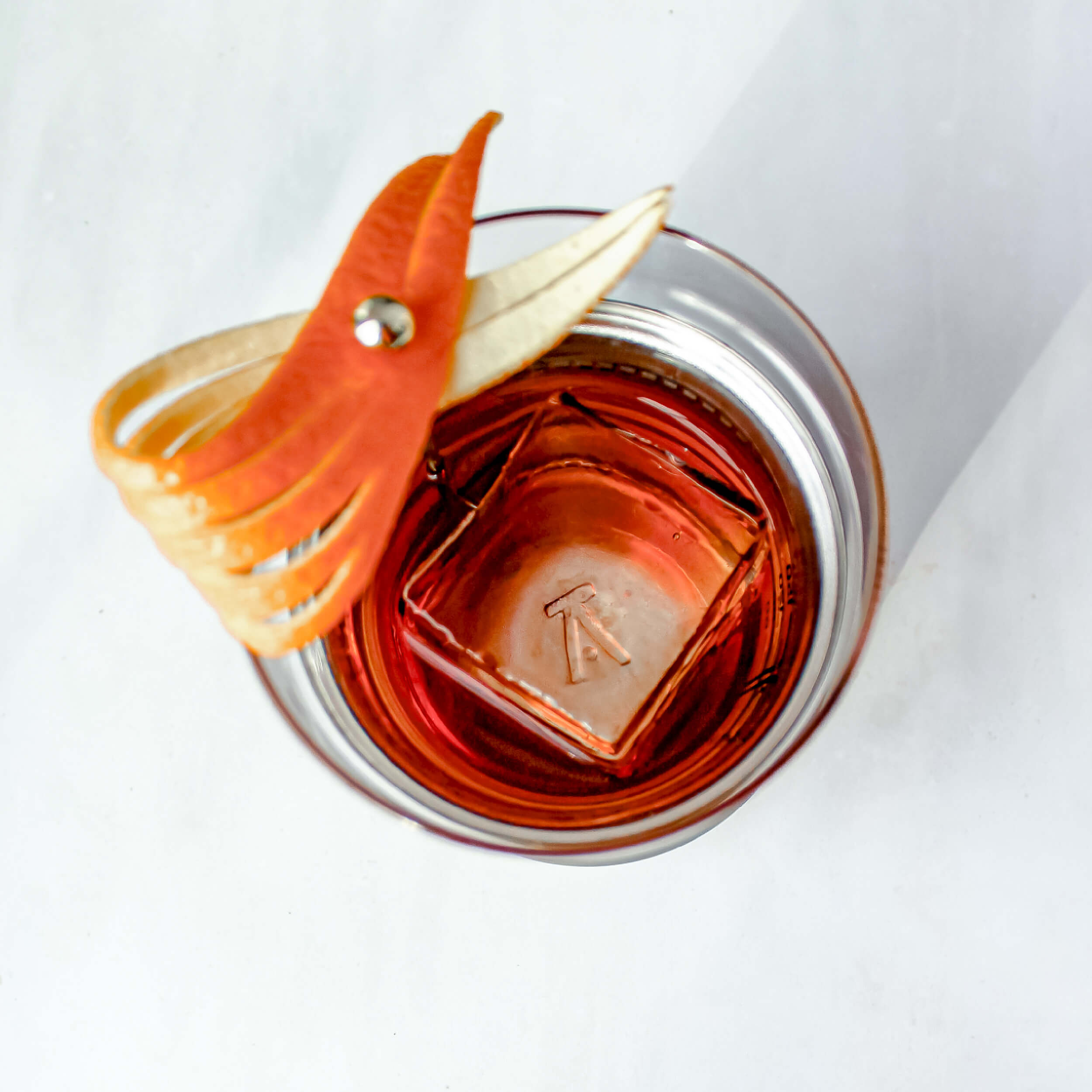 a brushed copper finish Hybrid Cocktail Glass viewed from above filled with a dark orange cocktail and single large ice cube garnished with an orange peel
