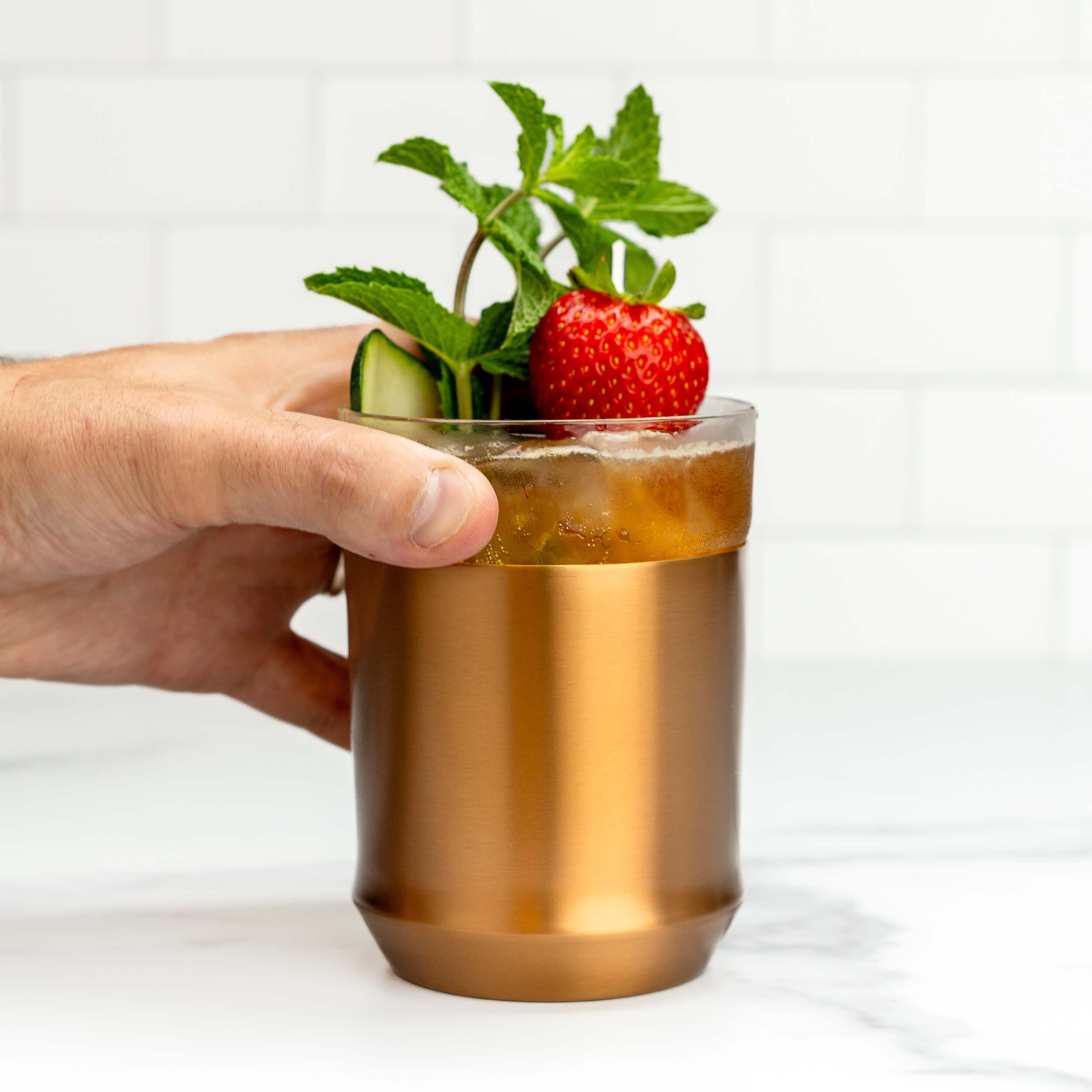 Elevated Craft Hybrid Cocktail Glass in brushed copper finish filled with an amber cocktail garnished with a strawberry a cucumber slice and a thick sprig of mint