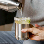 Brushed Stainless finish Hybrid Cocktail Shaker pouring a margarita into the Hybrid Cocktail Glass with a salted rim garnished with a lime wedge 