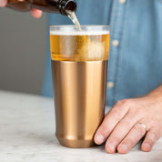 Person pouring cold beer from a bottle into the Elevated Craft Hybrid Pint Glass in brushed copper finish