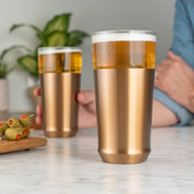 Elevated Craft Hybrid Pint Glass in brushed copper finish full of cold beer in foreground with a hand holding another brushed copper finish hybrid pint glass full of cold beer in the background