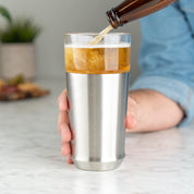 Man pouring cold beer from a bottle into the Elevated Craft Hybrid Pint Glass in brushed stainless finish