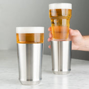 Elevated Craft Hybrid Pint Glass in brushed stainless finish full of cold beer in foreground with a hand holding a hybrid pint glass insert full of cold beer above the stainless steel base in the background