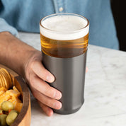 A man holding the Elevated Craft Hybrid Pint Glass in the gunmetal black finish filled with chilled full bodied beer on a marble surface